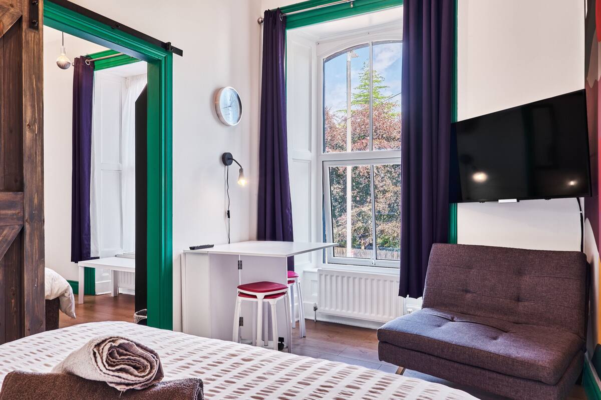 Una habitación con cama, escritorio, silla y ventana con cortinas.