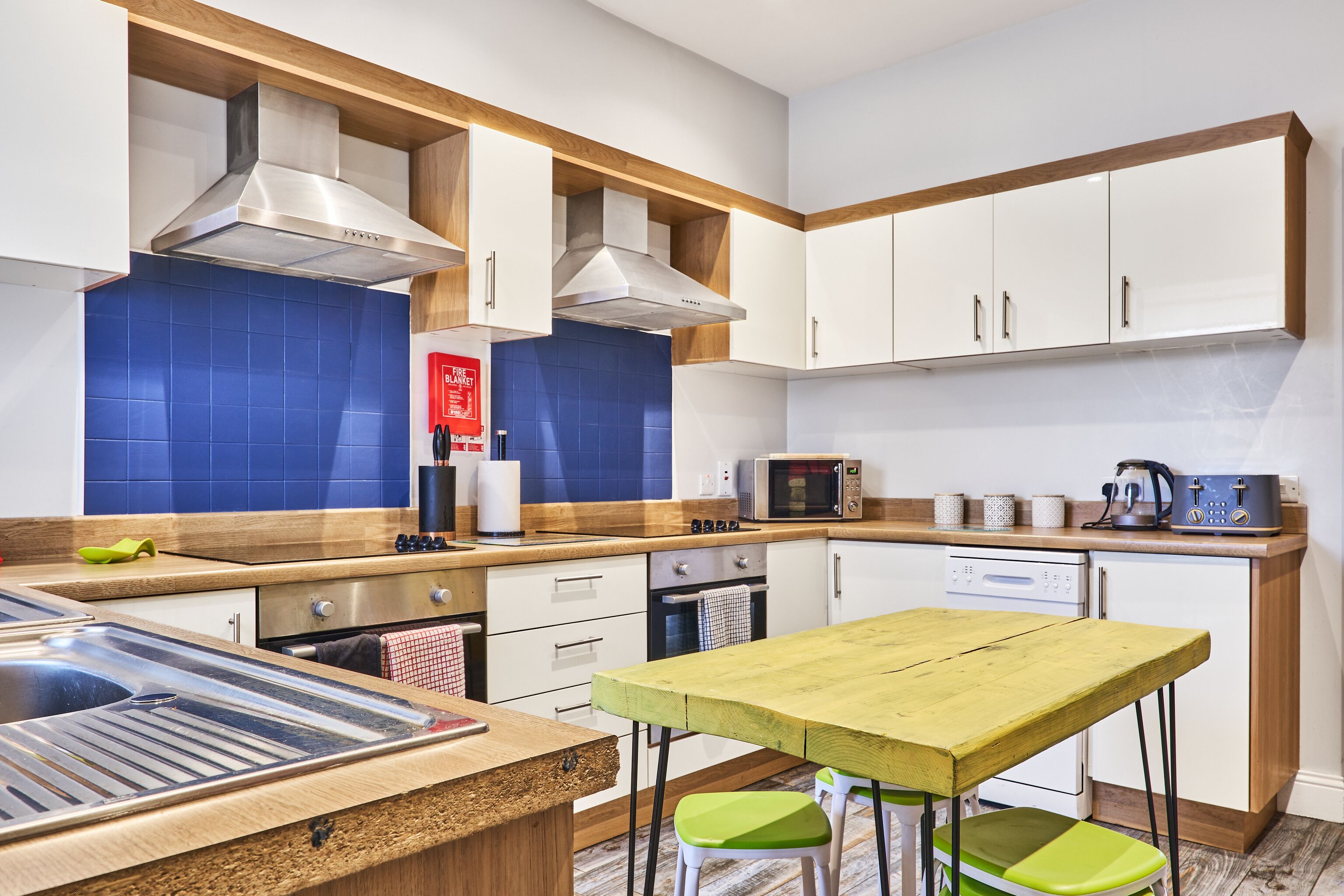 A modern kitchen with white cabinets, blue backsplash, stainless steel appliances, and a wooden table.