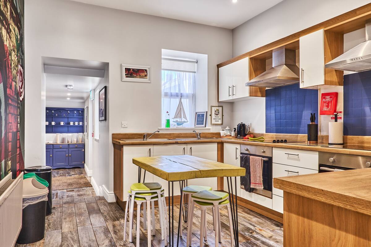 Una cocina moderna con una mesa de madera y taburetes, un backsplash de azulejos azules y una ventana con cortinas translúcidas.