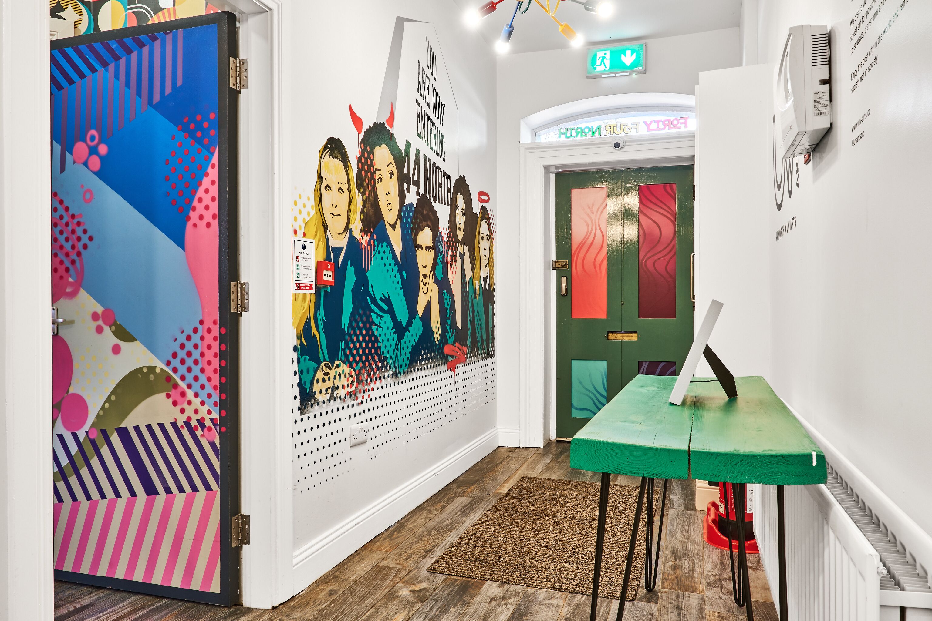 A hallway with colorful artwork, a green table, and a staircase.