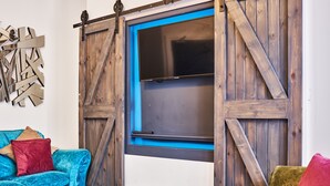 A room with a blue-framed window, a wooden table, a blue sofa, and a colorful armchair. - Forty Four North (Londonderry)