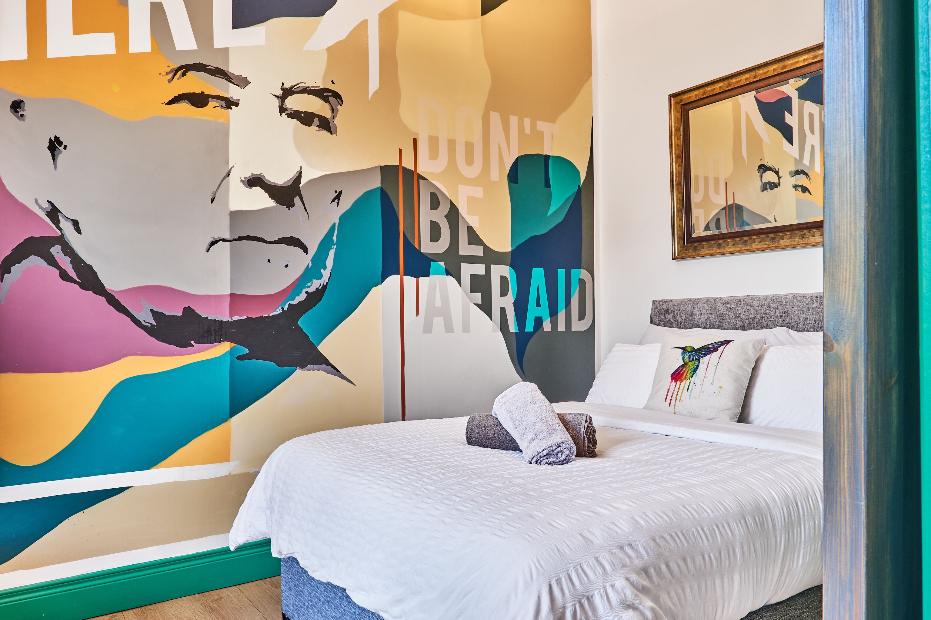 A bedroom with a large mural, a bed with white bedding, and a framed picture on the wall.