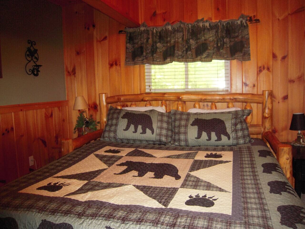 A wooden cabin bedroom with a bed featuring a bear-themed quilt and matching pillows.