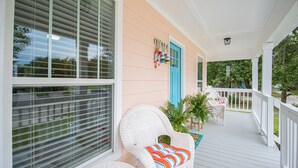 A covered porch with white wicker chairs, a blue door, and a view of the street. - Seas the Day Cottage (Gulfport)