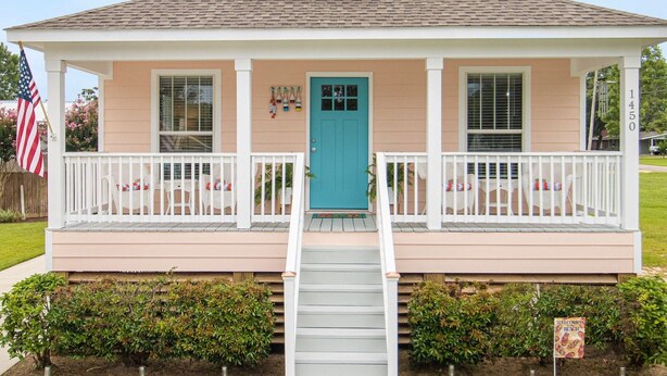 A two-story house with a front porch, a blue door, and a small staircase leading to the entrance. - Seas the Day Cottage (Gulfport)