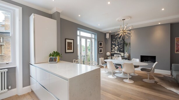 A modern kitchen with a marble island, a dining area with white chairs, and a fireplace. - Maida Vale Elegance (London)