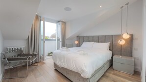 A modern bedroom with a large bed, bedside tables, a bench, and a view of the city. - Maida Vale Elegance (London)
