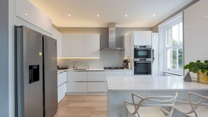 A modern kitchen with white cabinetry, stainless steel appliances, and a central island with bar stools. - Maida Vale Elegance (London)
