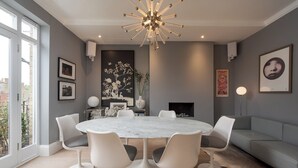 A modern dining room with a round marble table, white chairs, and a contemporary chandelier. - Maida Vale Elegance (London)