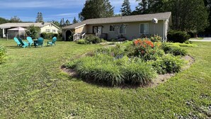 A residential house with a front porch, a covered patio with chairs, and a well-maintained lawn with flowers. - Welcome home in a welcoming town! (Littleton)