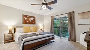 A bedroom with a bed, bedside lamps, a ceiling fan, a large window with curtains, and a view of greenery outside. - Quiet Mountain Home with Fireplace, A+ Location (Banner Elk)