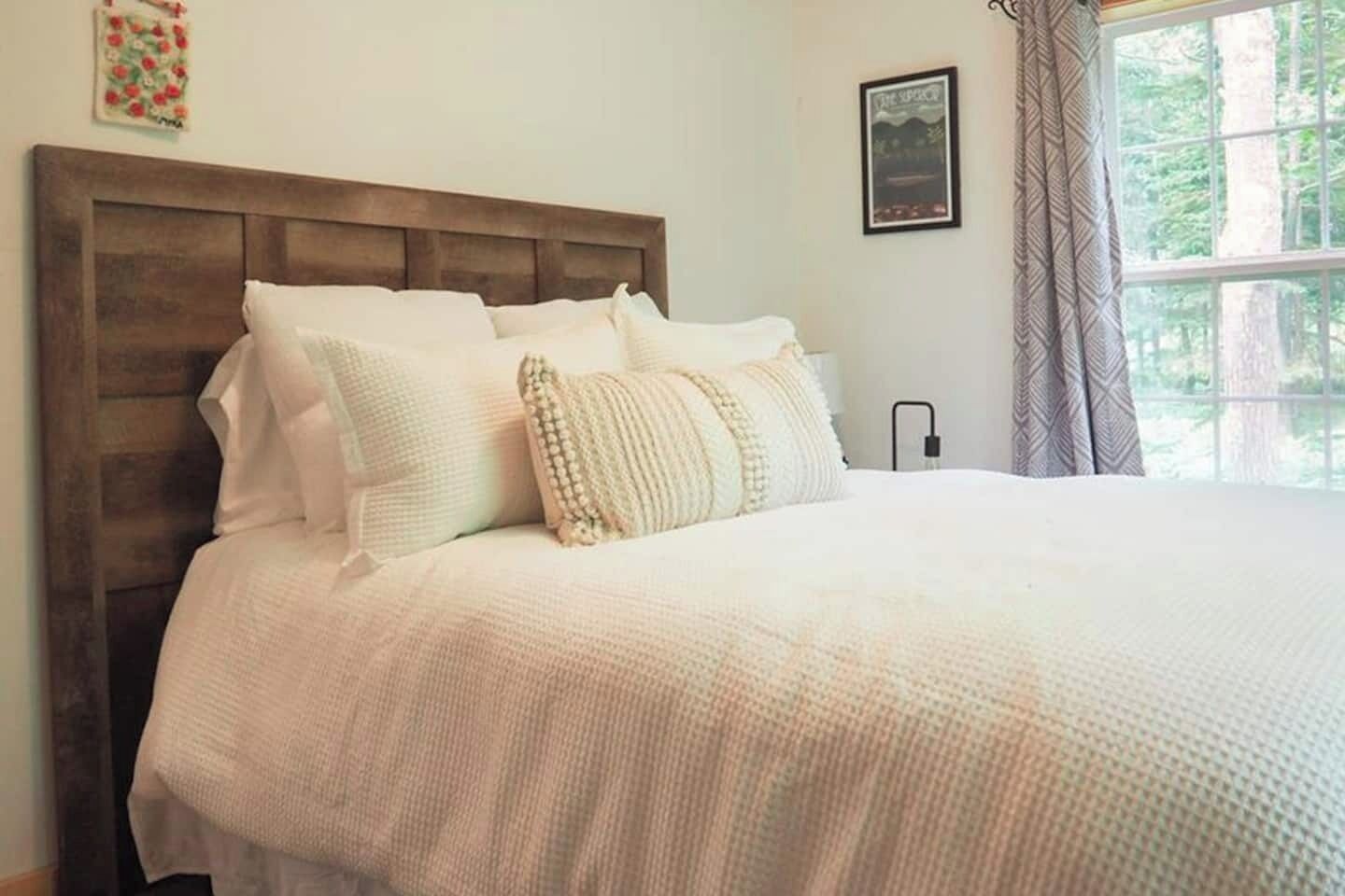 A neatly made bed with a wooden headboard, white bedding, and a bedside table with a lamp.