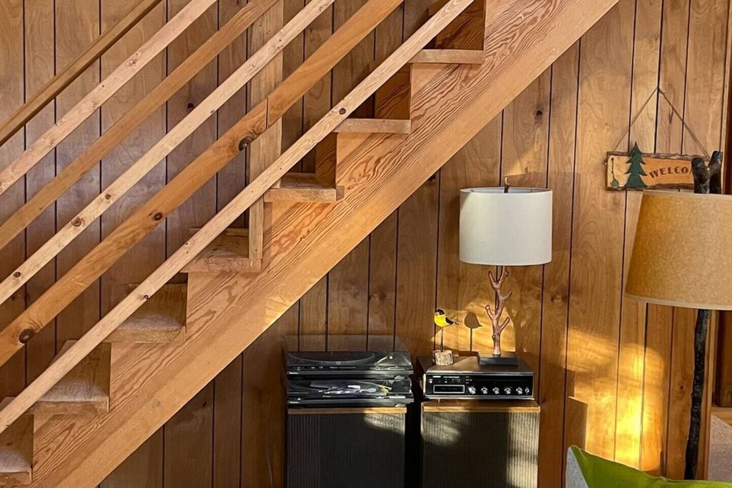 Un escalier en bois, avec une radio et une lampe d’époque posées sur un meuble en bois.