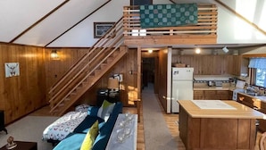 Een knus houten huisje van binnen, met een slaapkamer op een entresol, een keuken en een trap.