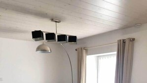 Una sala de estar moderna con un sofá azul, dos mesas redondas de madera y un televisor instalado en el techo.
