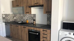 Una cocina compacta con armarios de madera, horno integrado, microondas y lavadora.