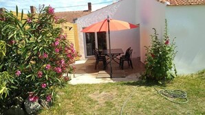 Un patio con una mesa y sillas, un paraguas rojo y un jardín con flores rosadas.