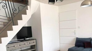 Una sala de estar moderna con un sofá gris, un televisor sobre un mueble blanco, una escalera y un sofá azul.