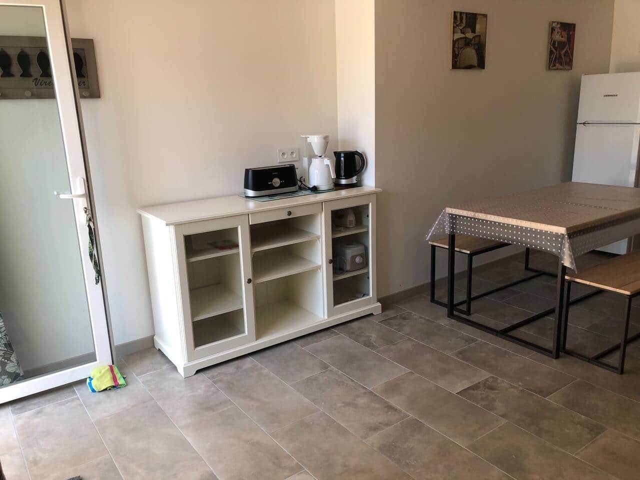 Une petite cuisine avec un meuble blanc, une machine à café et une table dotée d’un cadre en métal.