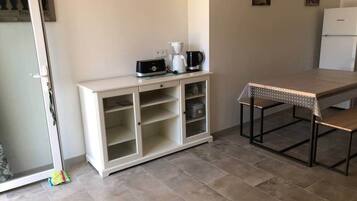 Une petite cuisine avec un meuble blanc, une machine à café et une table dotée d’un cadre en métal.