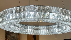 Un intérieur moderne agrémenté d’un grand lustre en cristal, d’un téléviseur et d’œuvres d’art accrochées aux murs.