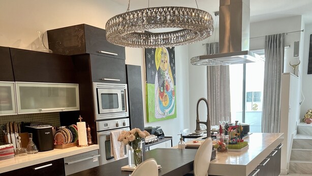 Une cuisine moderne avec un îlot central, des tabourets de bar, un luminaire suspendu et un chien sur le sol.