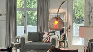 Un salon moderne avec un canapé gris, un lustre rond et une grande fenêtre avec des rideaux.