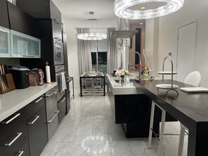 Een moderne keuken met een centraal eiland, roestvrijstalen apparatuur en een kroonluchter.