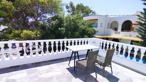 A balcony with a white railing, a table, and two chairs. - Perissa Art Villa - Kitchen & Washing Machine (Santorini)