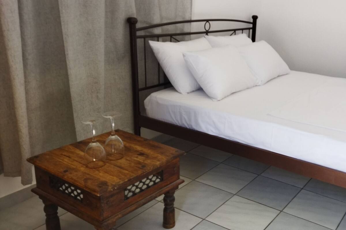 A bedroom with a wooden bed, white bedding, and a small wooden table with two wine glasses.