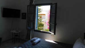 A bedroom with a bed, a TV mounted on the wall, a small table, and a window with curtains. - Perissa Art Villa - Kitchen & Washing Machine (Santorini)