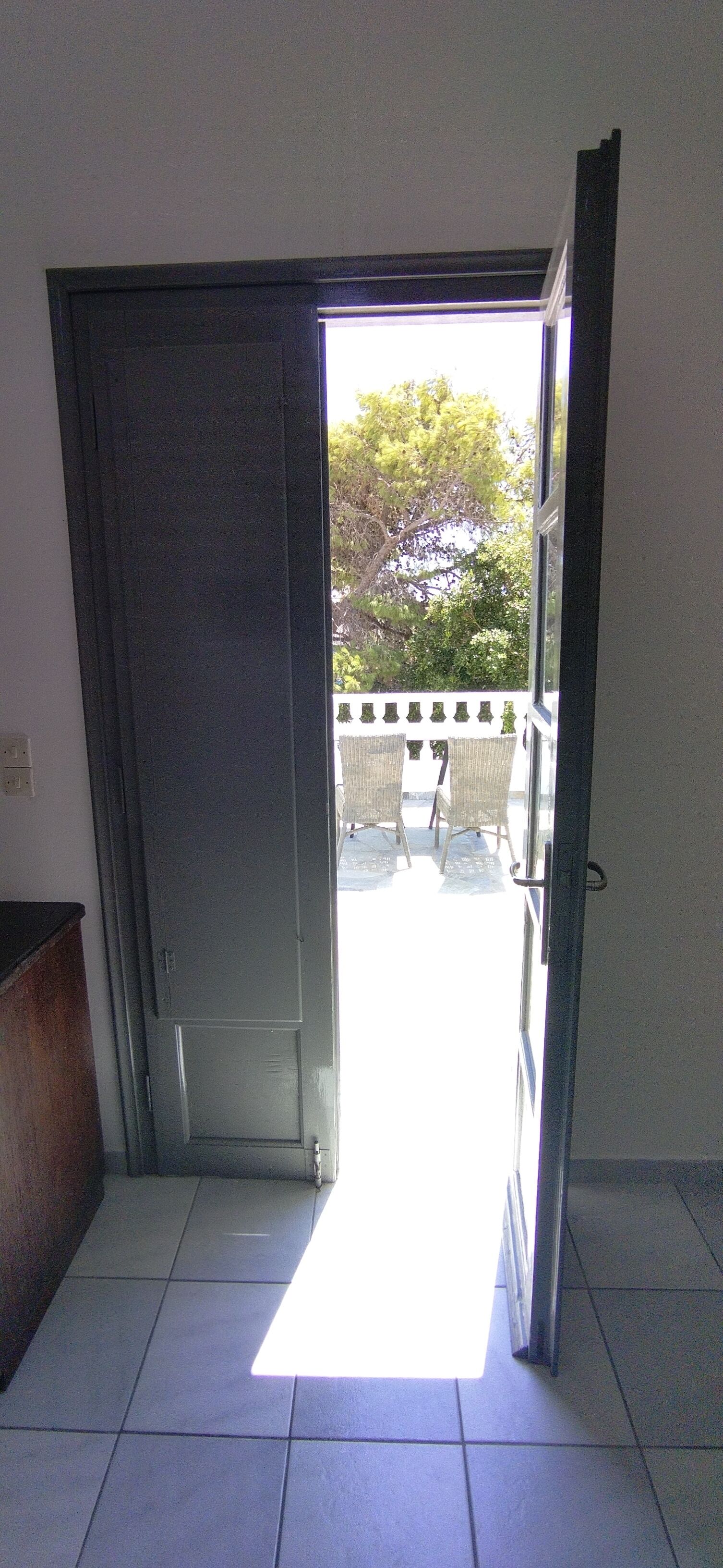 Puerta abierta que da a un espacio exterior con vistas a árboles y un patio con sillas.