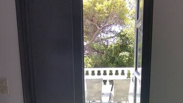 Puerta abierta que da a un espacio exterior con vistas a árboles y un patio con sillas.