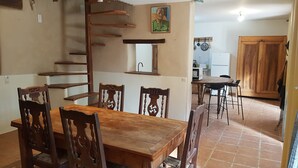 A dining area with a wooden table and chairs, a kitchen in the background, and a staircase leading to an upper level. - Isolated house set in vineyards and woods (VALADY)