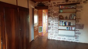 A hallway with wooden doors, a stone wall, and a bookshelf with books and decorative items. - Isolated house set in vineyards and woods (VALADY)