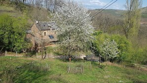 A stone house with a sloped roof, surrounded by blooming trees and a fenced garden. - Isolated house set in vineyards and woods (VALADY)