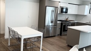 A modern kitchen with stainless steel appliances, a white dining area, and a wooden floor.