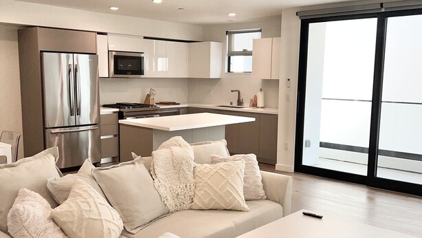 A modern living room with a sofa, a coffee table, and a kitchen area with a refrigerator and microwave.