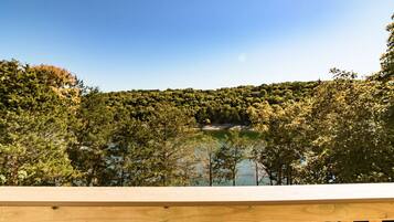 A wooden deck overlooking a lake with dense forest and a house on a hill in the background.