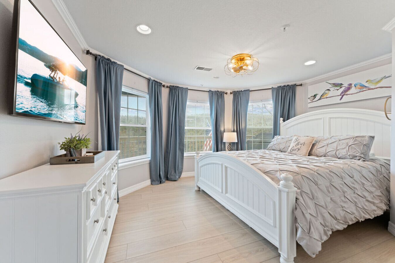 A bedroom with a bed, a dresser, a TV, and a window with curtains.
