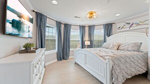 Un dormitorio con cama, cómoda, televisor y ventana con cortinas.