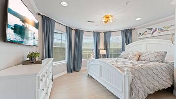 A bedroom with a bed, a dresser, a TV, and a window with curtains.