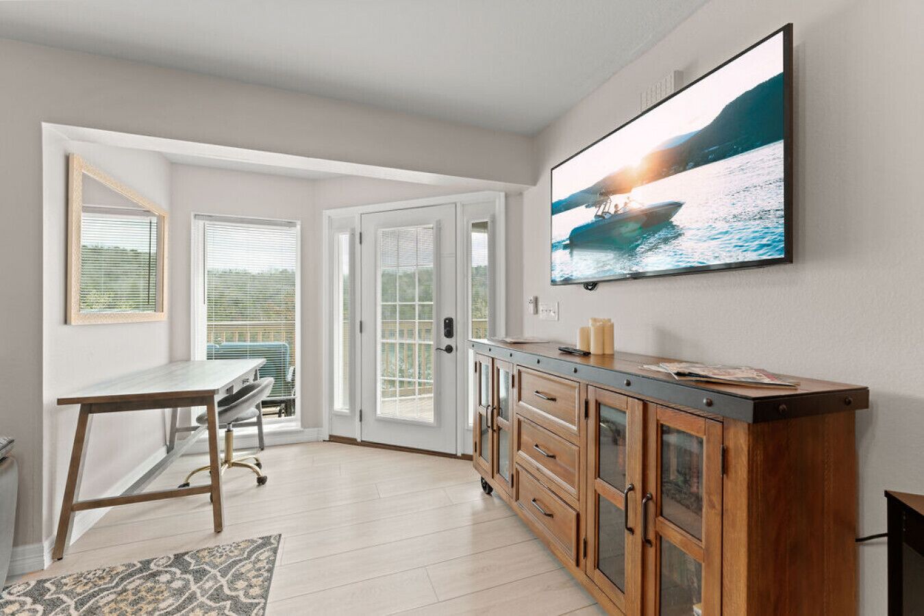 A modern kitchen with a dining area, wooden cabinets, a large TV, and a view of the sea.