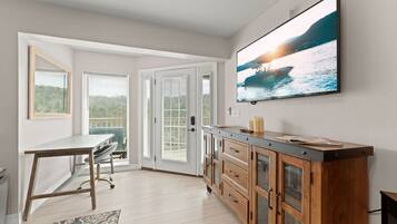 A modern kitchen with a dining area, wooden cabinets, a large TV, and a view of the sea.