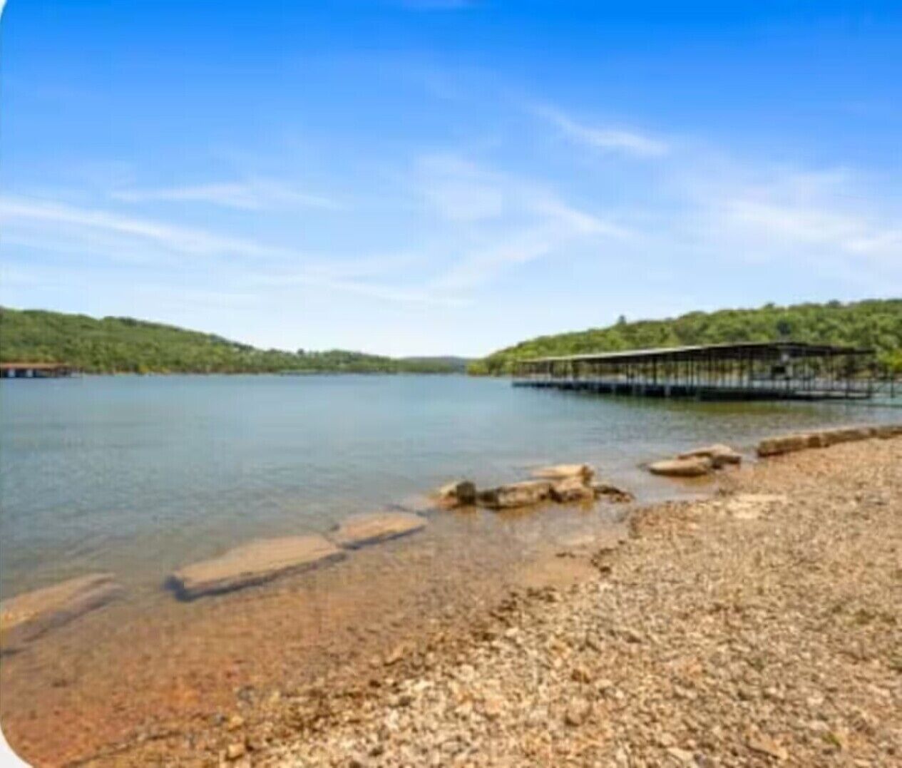 A calm lake with a wooden pier extending into the water, surrounded by hills.