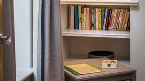 Ein Badezimmer mit Waschtisch, einem Spiegel mit Beleuchtung, einem Regal mit Büchern und einem kleinen Tisch mit einer Pflanze.