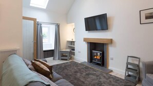 Ein gemütliches Wohnzimmer mit Kamin, einem flachbildfernseher darüber und einer komfortablen Sitzecke mit Sofa und Sessel.