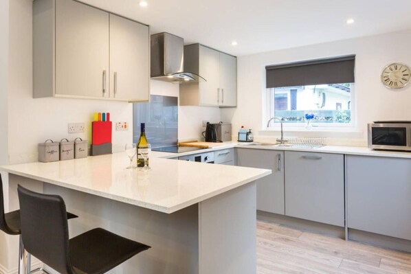 A modern kitchen with grey cabinets, a central island, a built-in oven, and a window with a view. - Ideal Couples Base for Exploring the Isle of Arran (Isle of Arran)