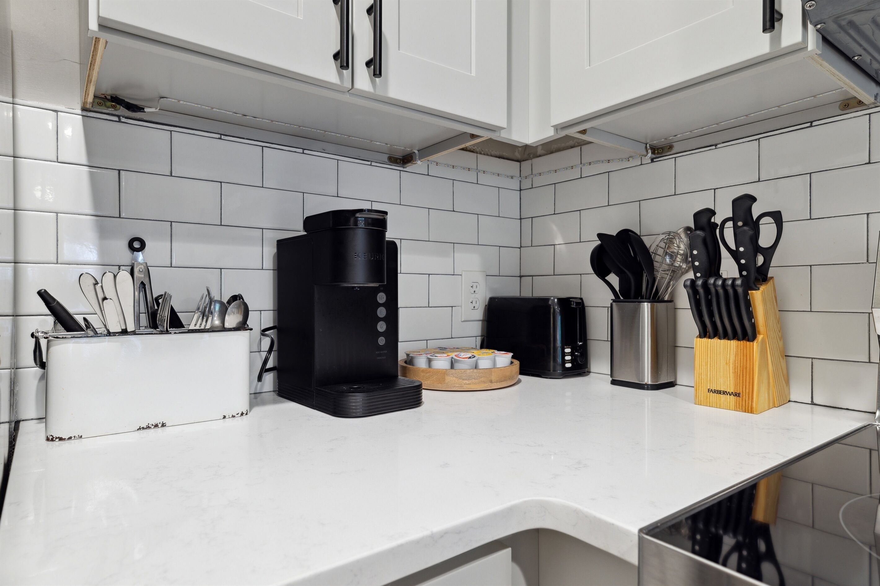 Una cocina con armarios blancos, una cafetera, un tostador y un bloque de cuchillos sobre la encimera.