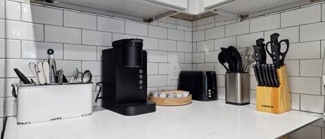 Una cocina con armarios blancos, una cafetera, un tostador y un bloque de cuchillos sobre la encimera.